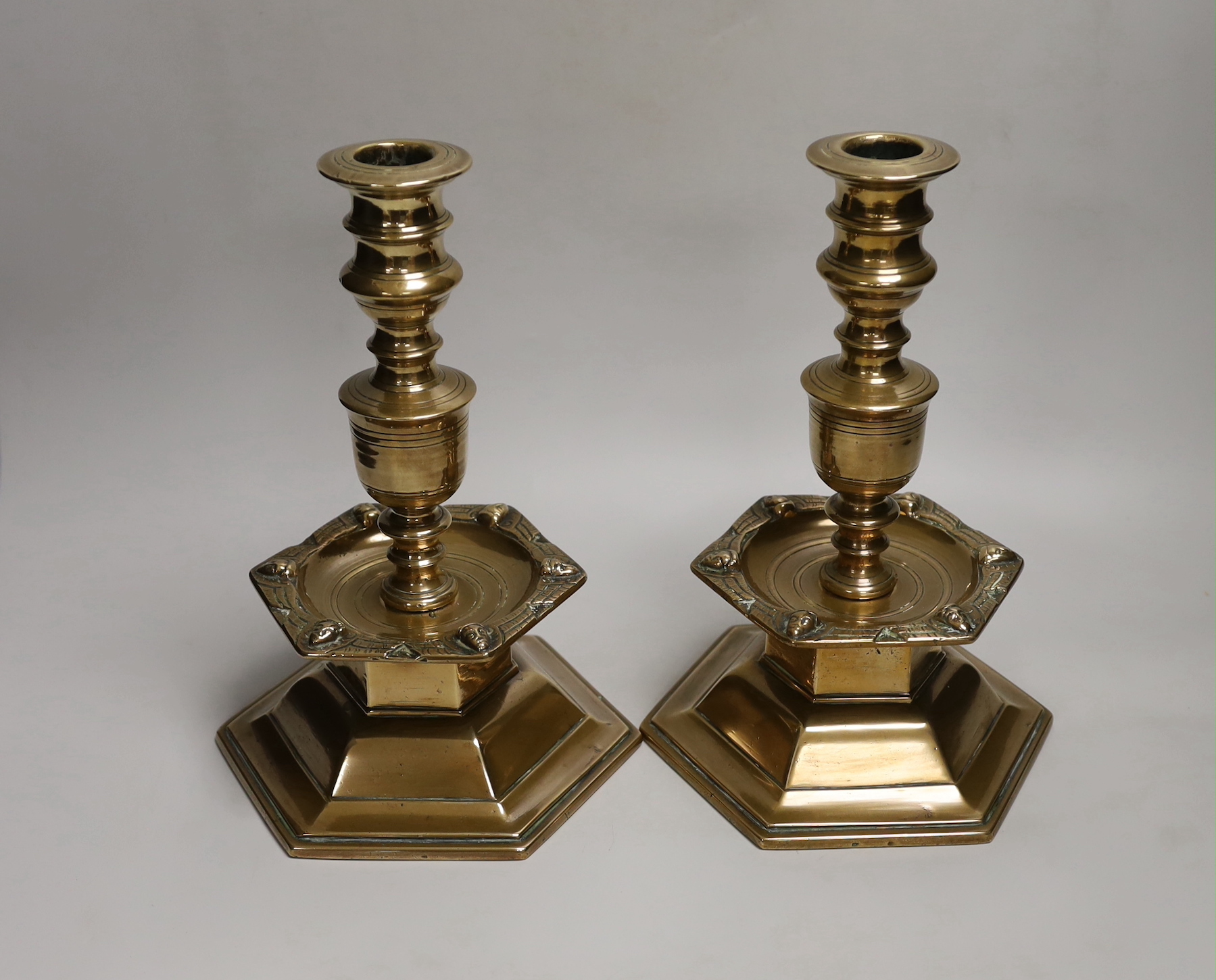 A pair of Scandinavian, possibly 17th century, brass candlesticks, dated 1644, each with a shield enclosing merchants mark, each with hexagonal base and hexagonal drip tray cast with marks, 27cm